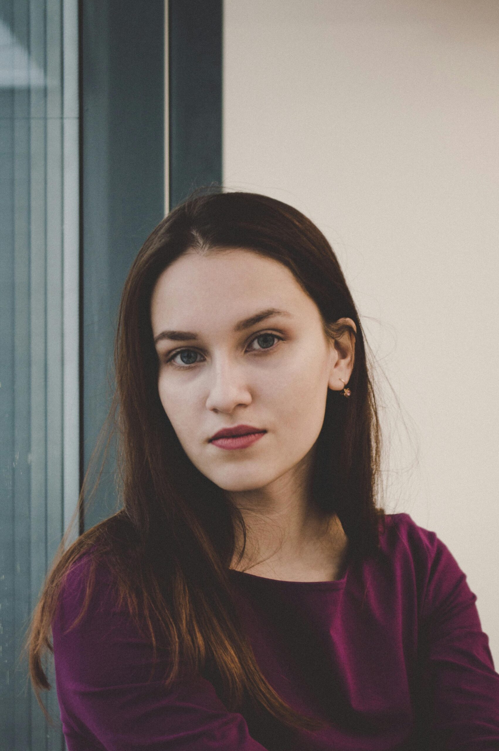 Portrait of a young woman with long brunette hair and a confident expression, looking towards the camera indoors.
